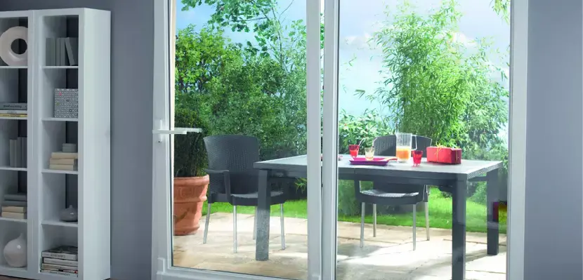 Une porte-fenêtre en PVC blanc donnant vers une terrasse aménagée