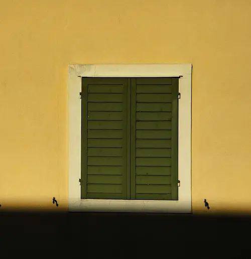 Un volet noir fermé le long d'un mur jaune.